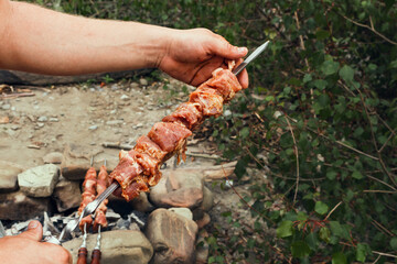Cooking a delicious shish kebab from raw meat on coals from a campfire, in the open air. The hands...