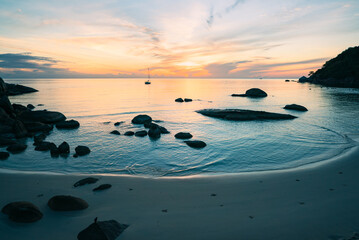 Fototapeta na wymiar Sea lagoon with cliffs and sandy beach at colorful sunrise. Sailboat in the sea.