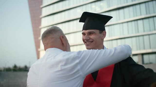 University graduation, a father embraces his son, a university graduate, young man in a graduate's robe holds a diploma in her hands, an emotional moment, handshake, 4k slow motion.