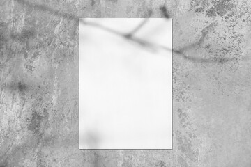 Empty white vertical rectangle poster or card mockup with soft tree leaves and branches shadows on neutral light grey concrete wall background. Flat lay, top view