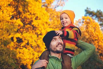 Cute little child boy sitting on his father's shoulders on background of beautiful autumn forest....