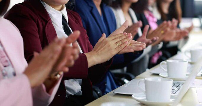 Group of businesswomen in suit sitting at working desk and clapping hands for appreciating to someone in modern office company. Concept of good circumstance in company with friends and colleagues.