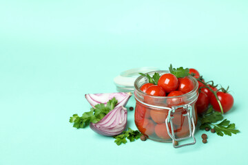 Jar with pickled tomatoes and ingredients on mint background