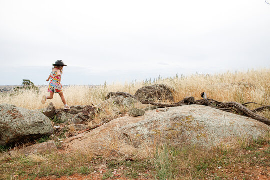 Distant shot of a young girl playing on rocky outcrop in grassy field
