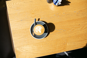 Top view shot of a coffee with an art in a small mug with a cup coaster and a teaspoon on a table