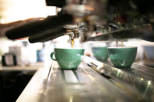 Close up shot of a coffee machine pouring coffee to a medium sized green mug on a coffee counter