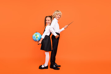 Photo of two schoolkids hold globe pointer direct empty space wear uniform isolated orange color background