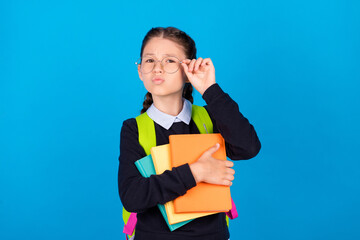 Photo of serious smart little girl wear glasses hold books wear backpack knowledge isolated on blue color background