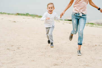 Mom with son running on the beach. Boy and mother walk on the seaside.