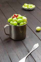 Metal mug with green gooseberries and red currants on top.
