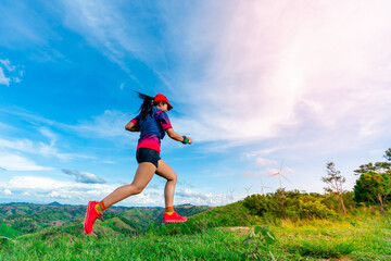 Asian female trail runners, wearing sportswear, are practicing running and jumping on the high mountain behind a beautiful view.. wind turbines generating electricity in the background.