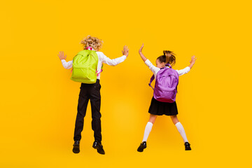 Fototapeta na wymiar Rear back view photo of funny positive kids jump wear backpack school uniform isolated yellow color background