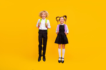 Photo of cheerful excited children jump have fun wear backpack school uniform isolated yellow color background