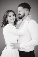 Groom with her lovely bride hug each other and make faces. Happy wedding couple in front of grey wall. Stuio photosession. Black and white photo