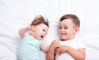 Fototapeta na wymiar happy little brother hugs his little sister lying on a white blanket