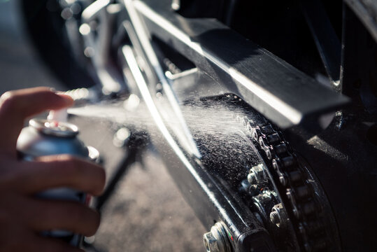 Detail of hand applying spray lubricant on motorcycle chain. Close-up photograph of oil droplets splashing.