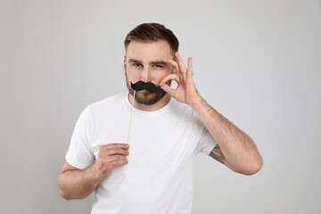 Funny man with fake mustache on light grey background