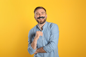 Funny man with fake mustache on yellow background