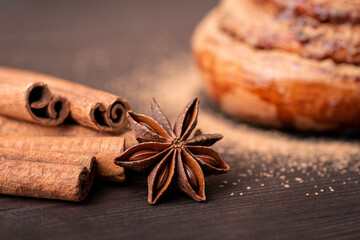 Obraz na płótnie Canvas Close-up shot of cinnamon sticks and anise star with a bun on the background. Cooking spicy bread with cinnamon