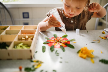 Cute child toddler glues leaves and petals at home, natural science in preschoolers, collecting...