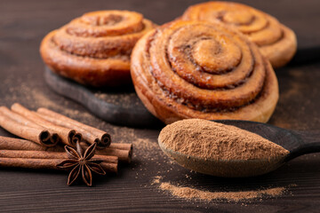 Homemade buns with cinnamon with some grounded spicies on wooden shoon. Coooking at home