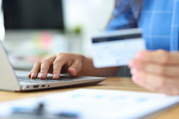 Businesswoman holds credit plastic card and dials number on laptop keyboard