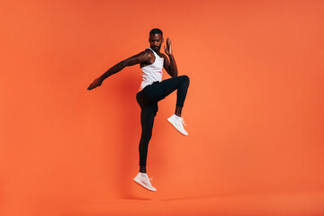 Fototapeta na wymiar Muscular athlete jumping in the air. Man in sports clothes doing fitness workout over orange background.