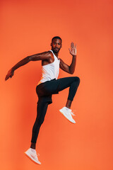 Fototapeta na wymiar Sportsman doing a stretching workout. Full length of healthy fitness man exercising against an orange background.
