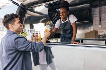 Food truck owner looking at customer. Smiling client receiving a drink from saleswoman.
