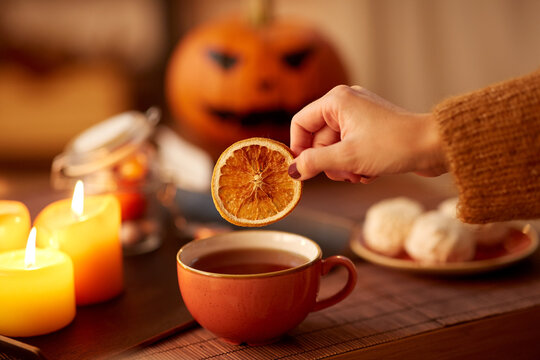 drinks, holidays and leisure concept - woman's hand adding dry orange slice to cup of tea at home on halloween