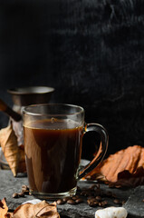 A glass mug of strongly brewed coffee on the stones with coffee beans and autumn leaves