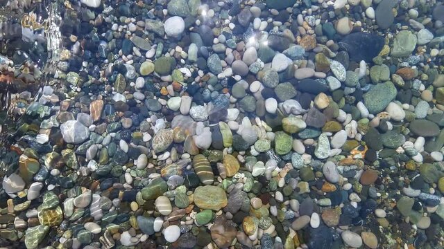Beautiful multi-colored pebbles under the transparent sea. Background, splash.