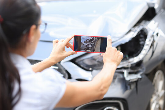 Woman agent takes pictures of damage to car after accident by smartphone