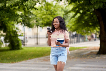 technology, education and people concept - happy smiling african american student girl with smartphone and book in city