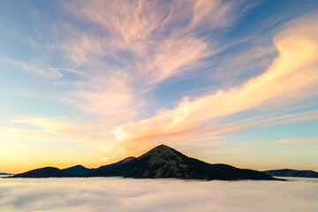 Aerial view of yellow sunset over white puffy clouds with distant mountains on horizon.