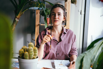 Young beautiful woman is sitting at work desk and holding a brush near her face. Searching ideas and inspiration concept.