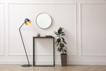 Console table, houseplant and lamp near light wall with mirror indoors. Interior design - obrazy, fototapety, plakaty