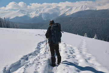 Fototapeta na wymiar Man backpacker hiking snowy mountain hillside on cold winter day.