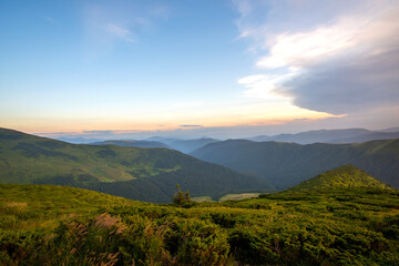 Summer evening mountain landscape with grassy hills and distant peaks at colorful sunset.