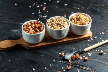 assorted peanuts with different seasonings for beer, on dark brown wooden background with copy...