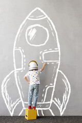 Happy kid draws a chalk rocket on the wall