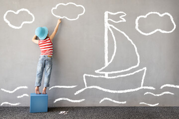 Happy kid draws a chalk ship on the wall