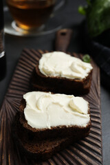 Bread with cream cheese on wooden board, closeup