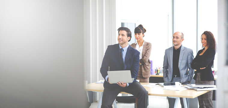 Business man holding laptop computer notebook and smiling at modern office with team.
