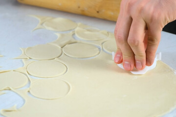 Man is cutting circles of dough for cooking dumplings using form, hands closeup