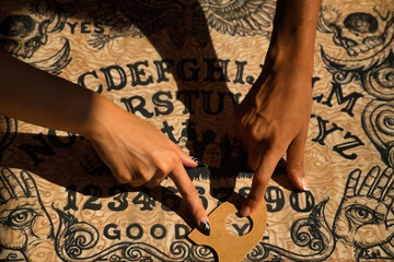 Detail of young Hispanic and Latina women's hands on a Ouija board signaling goodbye.