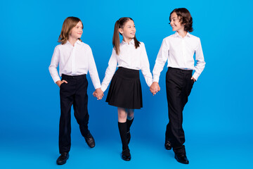 Photo of friendly classmates schoolkids hold hands walk enjoy wear uniform isolated blue color...