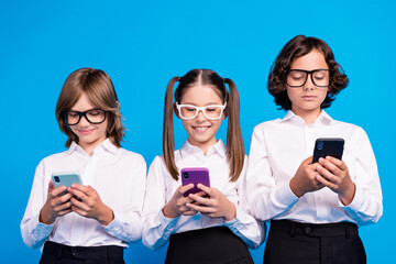 Photo of positive blogger schoolkids hold telephone typing sms wear glasses uniform isolated blue...