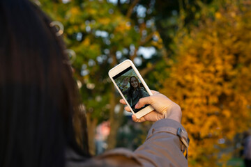 young woman having video chat  using  phone  camera  in the city park