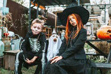 children a boy in a skeleton costume and a teenage girl in a witch costume having fun at a Halloween party on the decorated porch suburban house